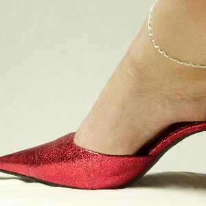 Close up of a foot in a red shoe wearing a sleek anklet.