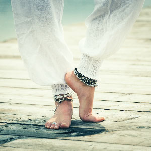 Legs in white trousers wearing jingling silver boho anklets.