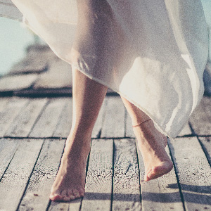 Close up of lady's legs in a floaty white dress wearing an anklet.