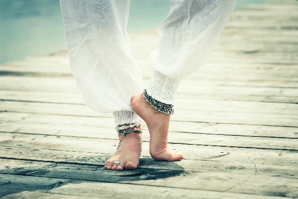 Legs in white trousers wearing jingling silver boho anklets.