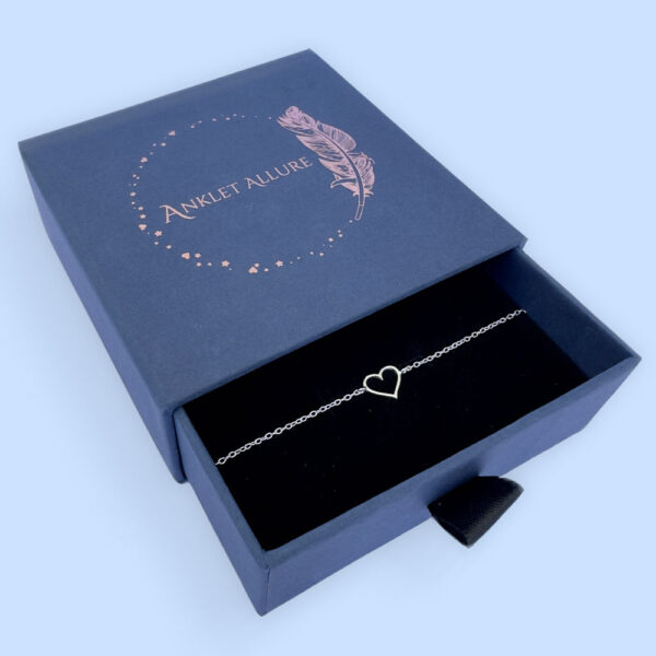 Sterling silver anklet with a simple hollow heart charm, presented in a blue jewellery box with Anklet Allure written on the top in rose gold.