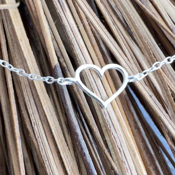 Silver heart charm on a silver anklet laying across straw.