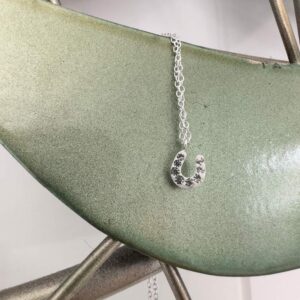 Horseshoe charm anklet on a light green metal background.