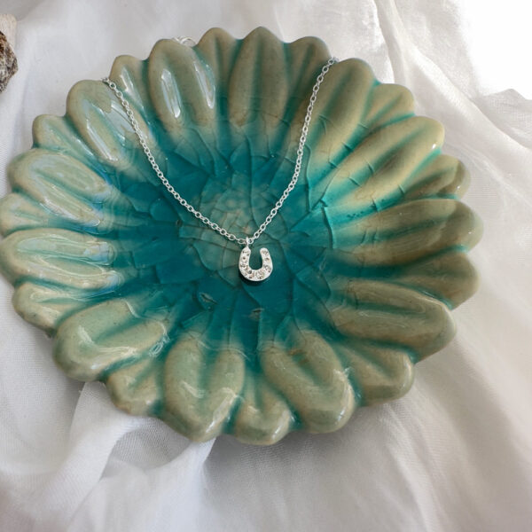 Horseshoe charm anklet on a turquoise flower shaped plate.