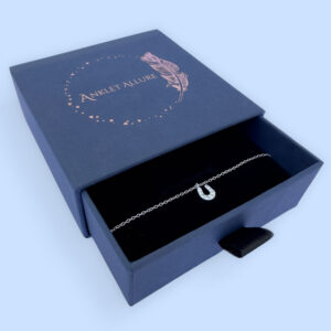 Sterling silver anklet with a horseshoe pendant with white gemstones, presented in a blue jewellery box with Anklet Allure written on the top in rose gold.