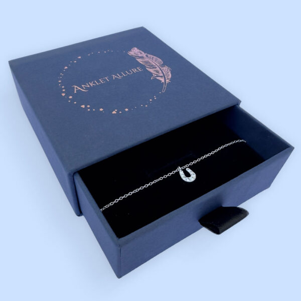 Sterling silver anklet with a horseshoe pendant with white gemstones, presented in a blue jewellery box with Anklet Allure written on the top in rose gold.