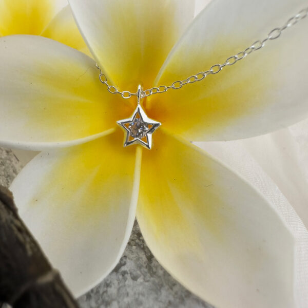 Close up of a silver anklet with silver star charm with a big cubic zirconia stone in the centre, displayed on a big white and yellow frangipani.