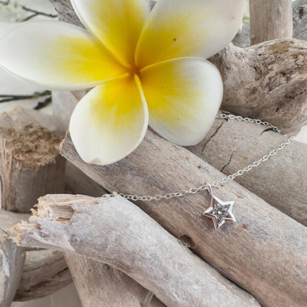 Stunning silver anklet with silver star charm with a big cubic zirconia stone in the centre, displayed on wood with a big white and yellow frangipani.