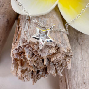 Stunning silver anklet with silver star charm with a big cubic zirconia stone in the centre, displayed on wood with a big white and yellow frangipani petal at the top of the photo.