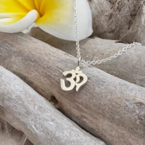 Silver anklet with an ohm symbol pendant presented on wood sticks with yellow and white frangipani flowers petal in top left corner.