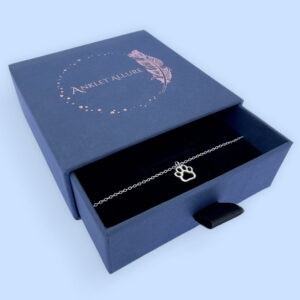 Cute silver anklet with a dog's pawprint charm, presented in a blue jewellery box with Anklet Allure written on the top in rose gold.
