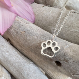 Cute puppy pawprint charm on a sterling silver anklet draped on some wood with a purple petal in the top left corner.