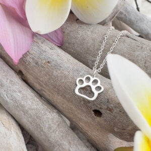 Silver pawprint charm on a silver ankle bracelet. Displayed on whitewashed sticks with frangipani petals around.