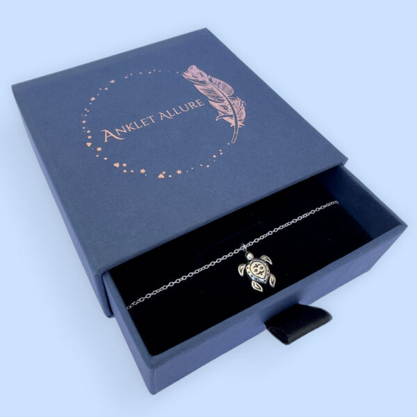 Tranquil anklet with a charm of a cute silver turtle, presented in a blue jewellery box with Anklet Allure written on the top in rose gold.
