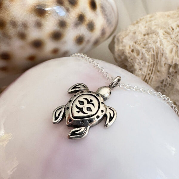 Patterned turtle charm on an anklet positioned on top of a white shell.