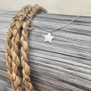 Sterling silver anklet with a silver star pendant draped over black and white wood with a twisted rope.