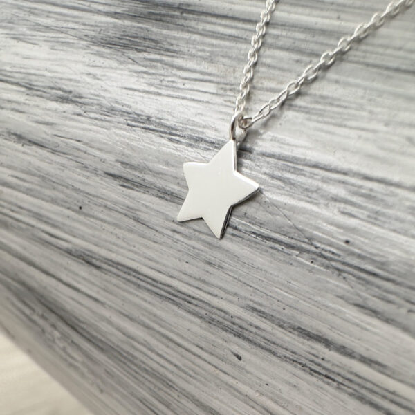 Solid silver dainty five pointed star charm on an anklet on a grey and white background.