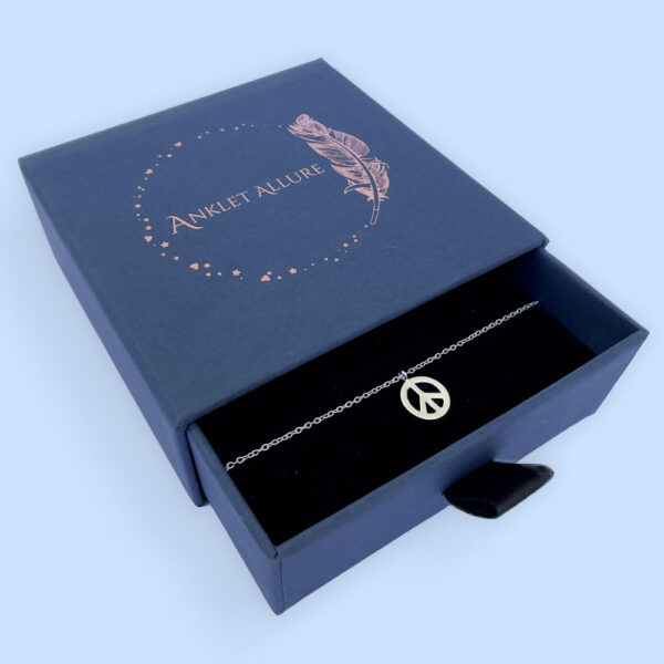 Beautiful peace symbol charm on a silver anklet, presented in a blue jewellery box with Anklet Allure written on the top in rose gold.