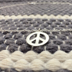 Silver anklet with a peace symbol charm on a blue and white wool background.