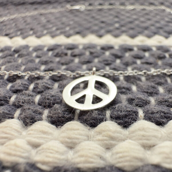 Silver anklet with a peace symbol charm on a blue and white wool background.