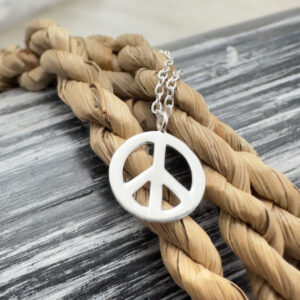 Close up of a peace sign anklet charm presented on a twisted rope.
