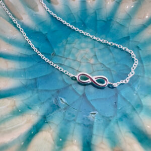 Sterling silver ankle bracelet with infinity charm laid on a turquoise plate.
