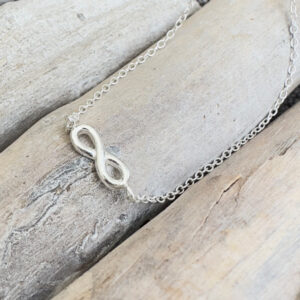 Sterling silver ankle bracelet with infinity charm, presented on wooden sticks.