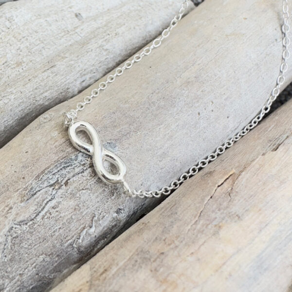 Sterling silver ankle bracelet with infinity charm, presented on wooden sticks.