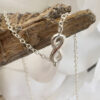 Silver anklet with infinity charm draped over some driftwood.