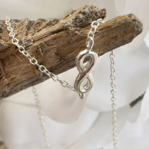 Silver anklet with infinity charm draped over some driftwood.