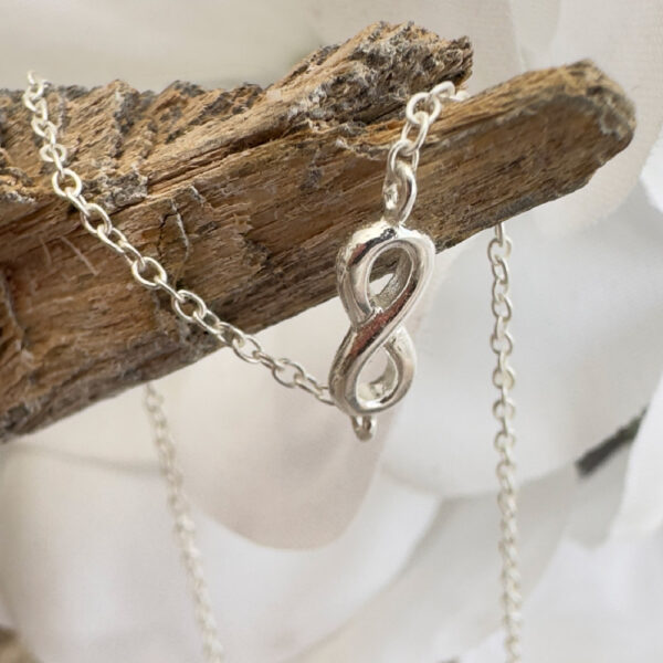 Silver anklet with infinity charm draped over some driftwood.