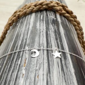 Silver anklet with a dainty moon and a dainty star draped over black and white lined wood.