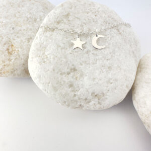 Dainty star and a crescent moon silver pendant on an anklet displayed on a white rock.