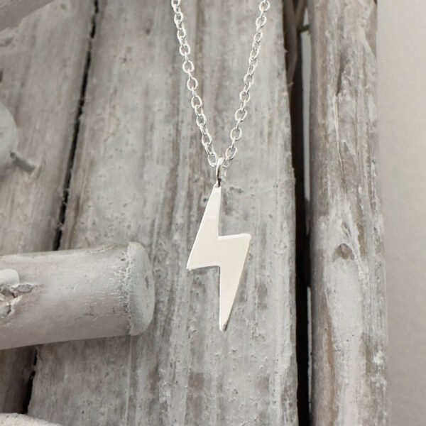 Anklet in 925 sterling silver with a shiny silver lightning bolt pendant hanging from a wood background.