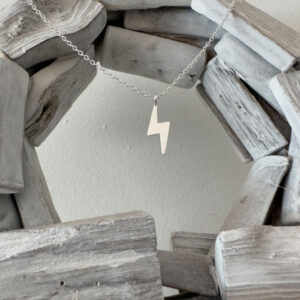 Silver anklet with a lightning bolt charm hanging between a wooden circle.