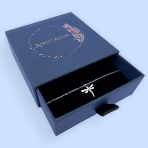 Eye catching silver anklet of a dragonfly with cubic zirconia stones, presented in a blue jewellery box with Anklet Allure written on the top in rose gold.
