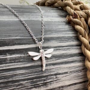 Beautiful sterling silver dragonfly charm on a black and grey wooden background.