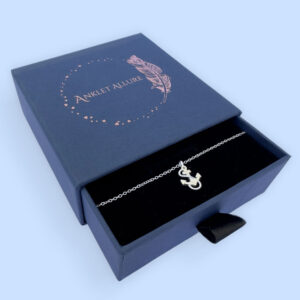 Silver anklet with a charm of an anchor with a rope around it, presented in a blue jewellery box with Anklet Allure written on the top in rose gold.