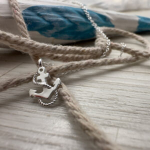 Close up of a sterling silver charm of an anchor with a rope curled around it, displayed on a rope.
