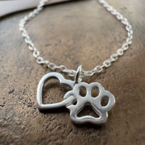 Close up of a sterling silver anklet with a heart linked to a pawprint charm.