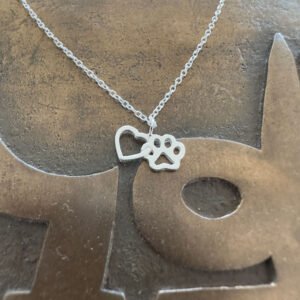 Close up of a sterling silver heart and pawprint charm interlinked together on an ankle bracelet on a gold background.
