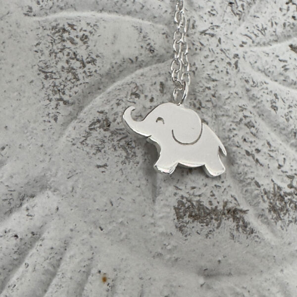 Close up of a cute shiny silver elephant charm on a sterling silver ankle chain on a white washed background.