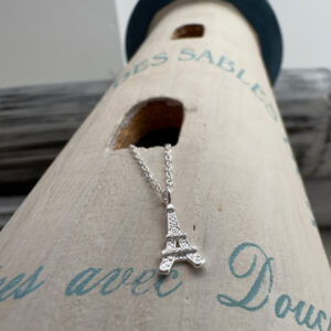 Eiffel Tower charm on a silver ankle bracelet laying on a lighthouse decoration.