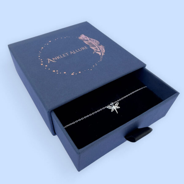 Feminine and captivating anklet with a silver dragonfly charm, presented in a blue jewellery box with Anklet Allure written on the top in rose gold.