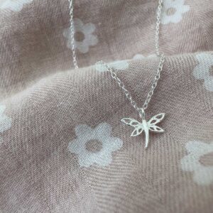 Beautiful dragonfly charm on a sterling silver ankle bracelet on a pink and white daisy fabric.
