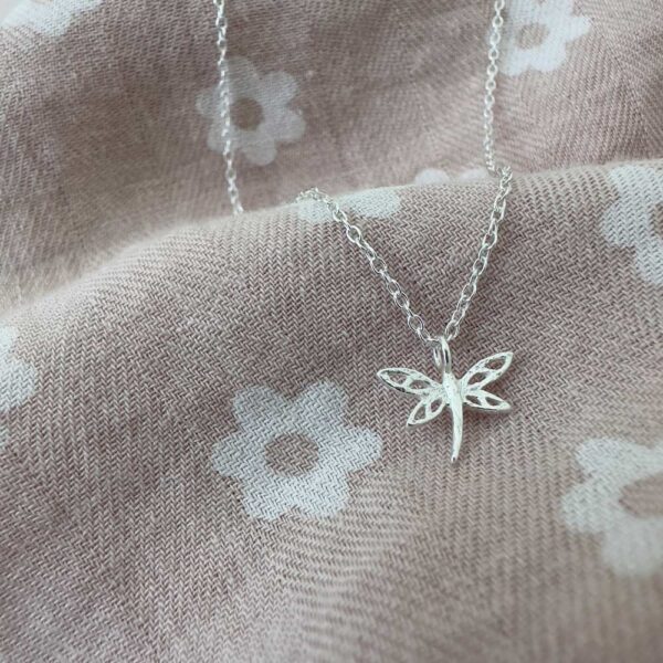 Beautiful dragonfly charm on a sterling silver ankle bracelet on a pink and white daisy fabric.