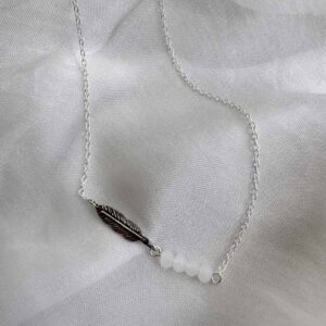 Silver ankle bracelet with an oxidised silver feather charm attached to four white beads.