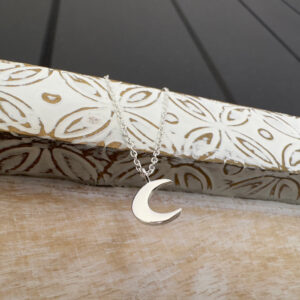 Silver ankle bracelet with crescent moon charm hanging from a white washed wood.