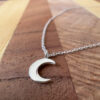 Crescent moon on a silver ankle bracelet on a wooden background.
