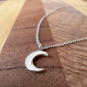 Crescent moon on a silver ankle bracelet on a wooden background.